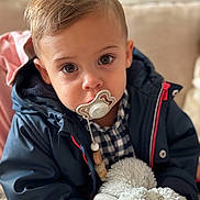 Loan participe au concours pour gagner de l'argent avec cette photo : toddler, pacifier, stuffed_animal, jacket, child, face, indoor, plush_toy, couch, warm_clothing, portrait, young_child, cute, baby, person, closeup, soft_lighting, expression, comfort, home