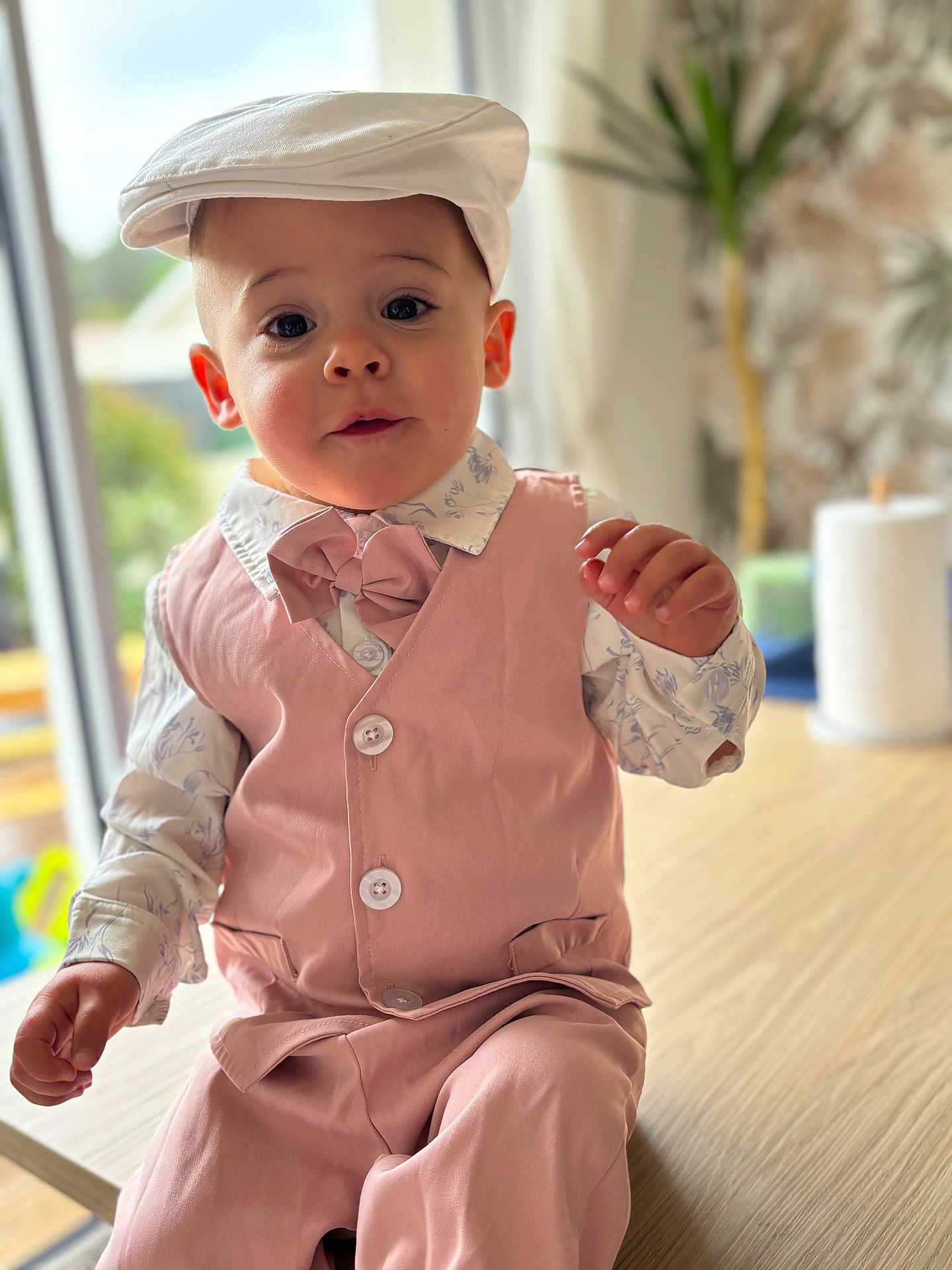 Loan a rejoint le concours — aidez-le/la à gagner de superbes lots ! toddler, child, boy, pink_vest, bow_tie, cap, portrait, indoor, table, curious_expression, clothing, face, hands, casual, fashion, cute, home, window, plant, blurred_background