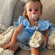 Lyha a rejoint le concours — aidez-le/la à gagner de superbes lots ! toddler, child, pacifier, blue_dress, blanket, couch, white_shoes, indoor, person, face, sitting, soft_texture, beads, clothing, footwear, comfort, young_child, cute, portrait, home