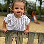 toddler, child, playground, fence, smiling, white_clothing, outdoor, sand, slide, wood, hair_tie, earrings, happy, person, nature, daylight, cute, portrait, casual, young