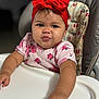Mía is registered to the contest to win money with this photo: baby, child, high_chair, red_bow, headband, pink_shirt, floral_pattern, cute, portrait, indoor, infant, expression, reaching, table, seat, person, skin, face, hand, toddler
