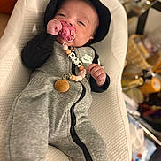 Rym participe au concours pour gagner de l'argent avec cette photo : baby, pacifier, onesie, hat, baby_seat, beaded_clip, indoor, infant, clothing, cute, comfortable, relaxed, pink, grey, black, person, portrait, young_child, toy, accessory