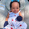 baby, smiling, infant, blue_bows, curly_hair, floral_outfit, mittens, baby_seat, plush, comfortable, sunlight, happy, portrait, child, cute, clothing, outdoor, closeup, person, relaxing