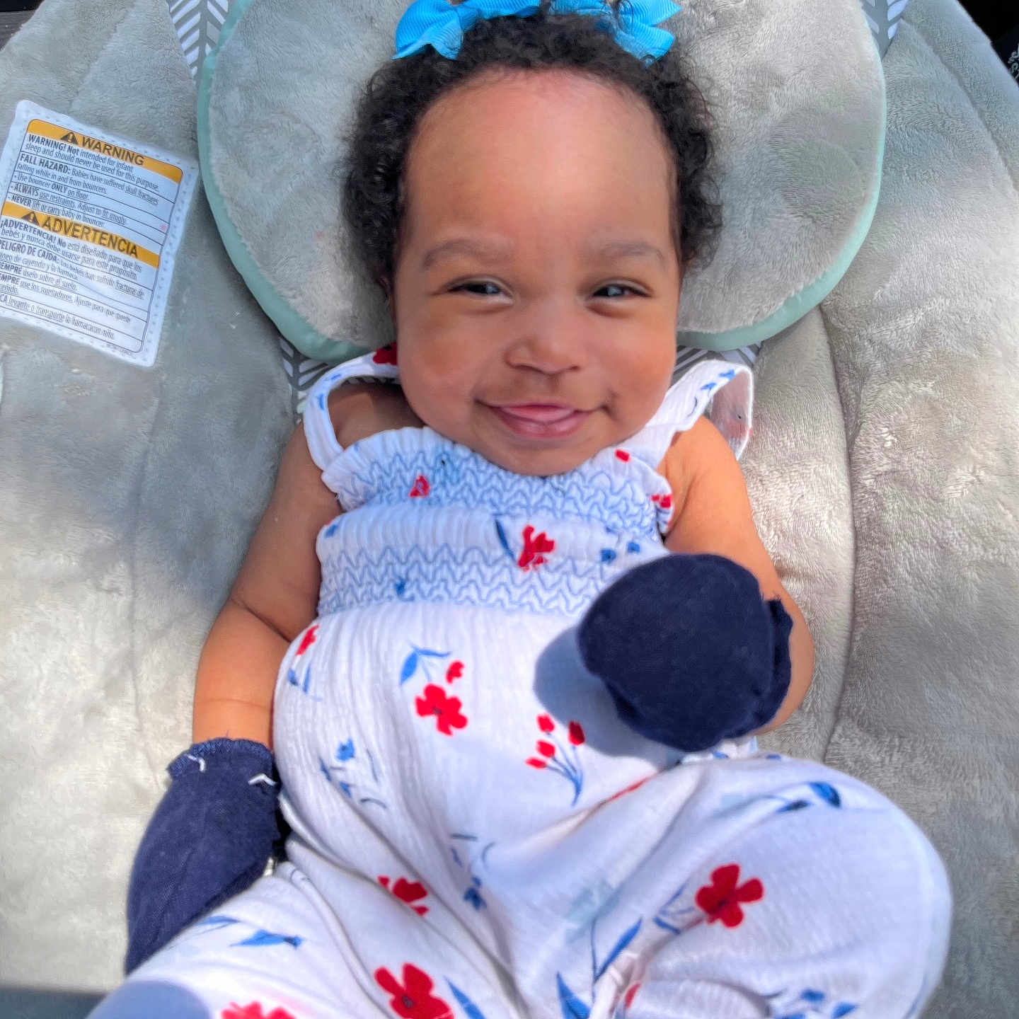 Sadie is registered to the contest to win money with this photo: baby, smiling, infant, blue_bows, curly_hair, floral_outfit, mittens, baby_seat, plush, comfortable, sunlight, happy, portrait, child, cute, clothing, outdoor, closeup, person, relaxing