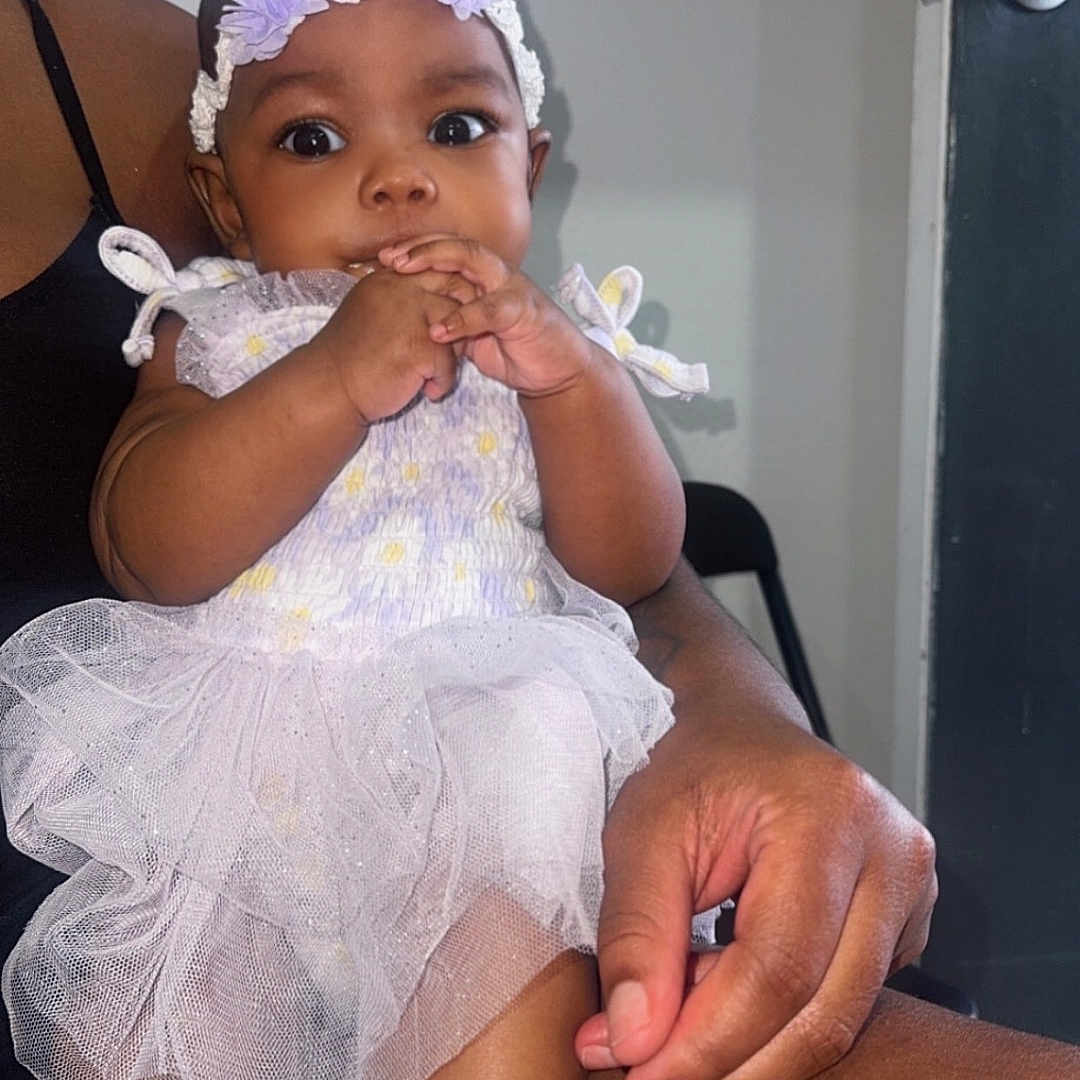 Bloom joined the competition — help win amazing prizes! adult, baby, chair, child, closeup, curious, cute, door, dress, flower, hand, headband, indoor, infant, lap, person, purple, seated, skin, socks