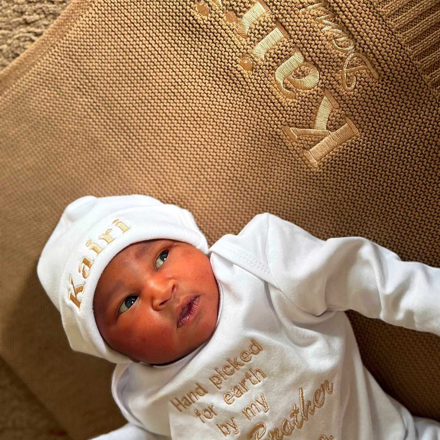 Kairi joined the competition — help win amazing prizes! newborn, baby, infant, child, portrait, lying_down, white_outfit, white_hat, couch, upholstery, indoor, face, eyes, mouth, clothing, embroidery, text_on_clothing, brown_background, soft_lighting, photography