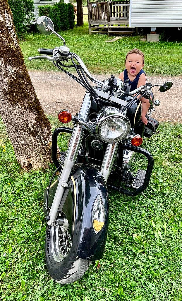 Emilio a rejoint le concours — aidez-le/la à gagner de superbes lots ! alloy_wheel, automotive_design, automotive_exhaust, automotive_exterior, automotive_lighting, automotive_tire, fender, fuel_tank, grass, headlamp, motor_vehicle, motorcycle, motorcycle_accessories, motorcycling, person, plant, rim, tire, vehicle, wheel