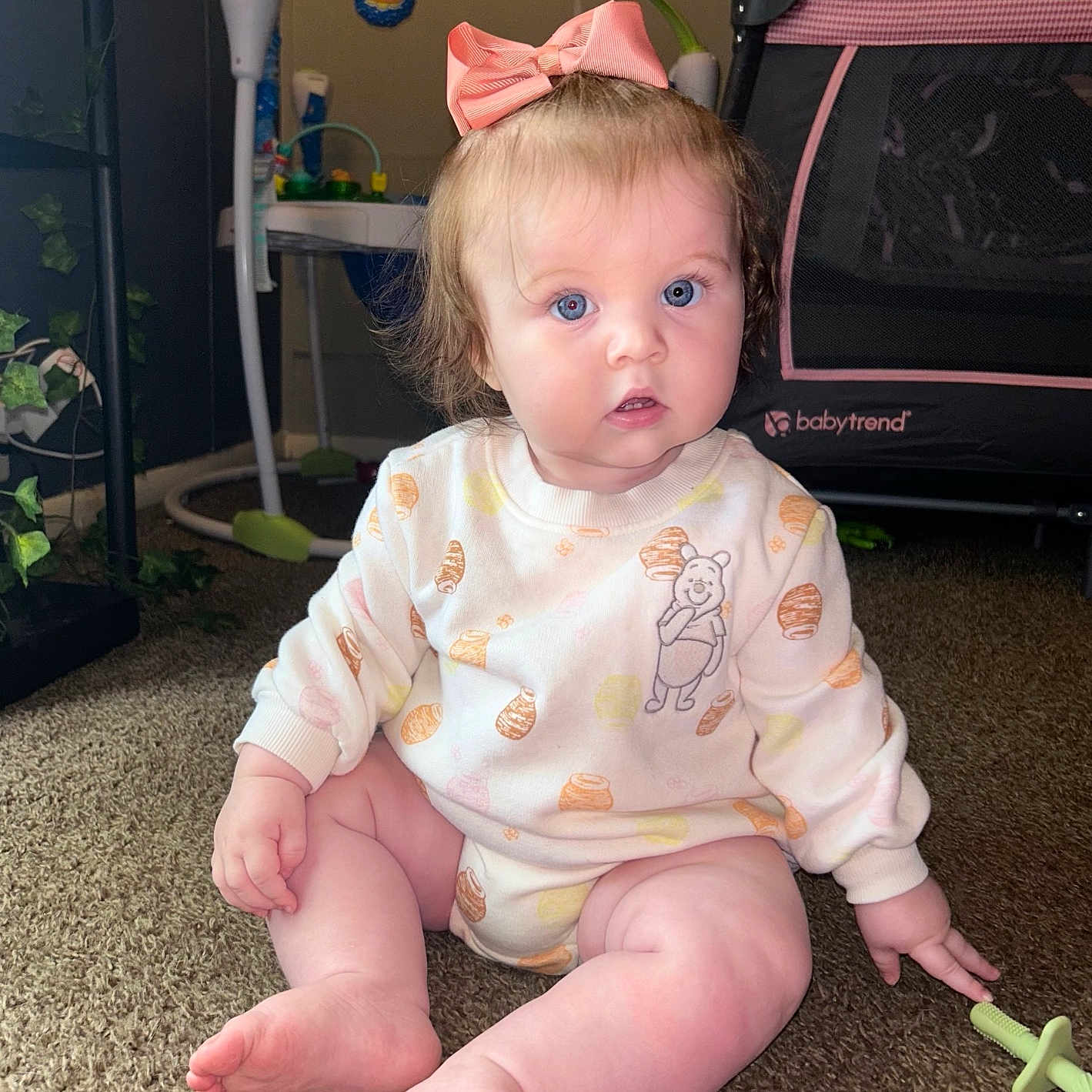 Octavia is registered to the contest to win money with this photo: baby, blue_eyes, bow, carpet, child, clothing, couch, face, floor, furniture, indoor, infant, nursery, outfit, pink_bow, playpen, sitting, toy, winnie_the_pooh, young_child