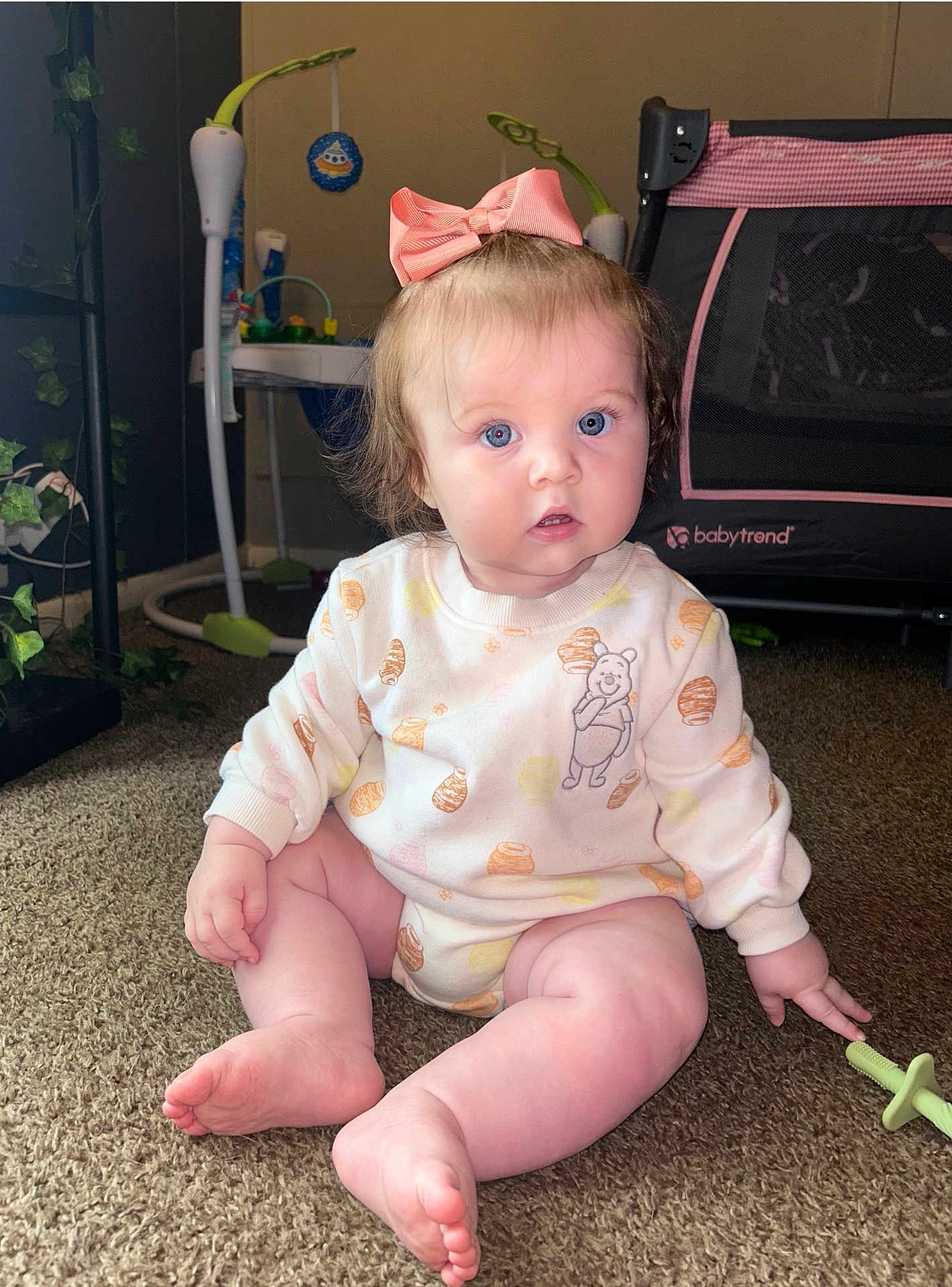 Octavia is registered to the contest to win money with this photo: baby, child, bow, blue_eyes, carpet, clothing, couch, face, floor, furniture, indoor, infant, nursery, outfit, playpen, sitting, toy, winnie_the_pooh, young_child, pink_bow