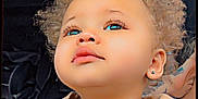 Deair is registered to the contest to win money with this photo: child, curly_hair, blue_eyes, beige_jacket, zipper, portrait, close_up, face, cute, baby, earrings, looking_up, indoor, dark_background, heart_graphic, casual_clothing, young_child, adorable, skin, fashion