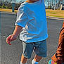 toddler, child, curly_hair, white_tshirt, shorts, socks, walking, holding_hand, adult_hand, outdoor, asphalt, road, blue_sky, flag, trees, daytime, casual_clothing, person, footwear, playful