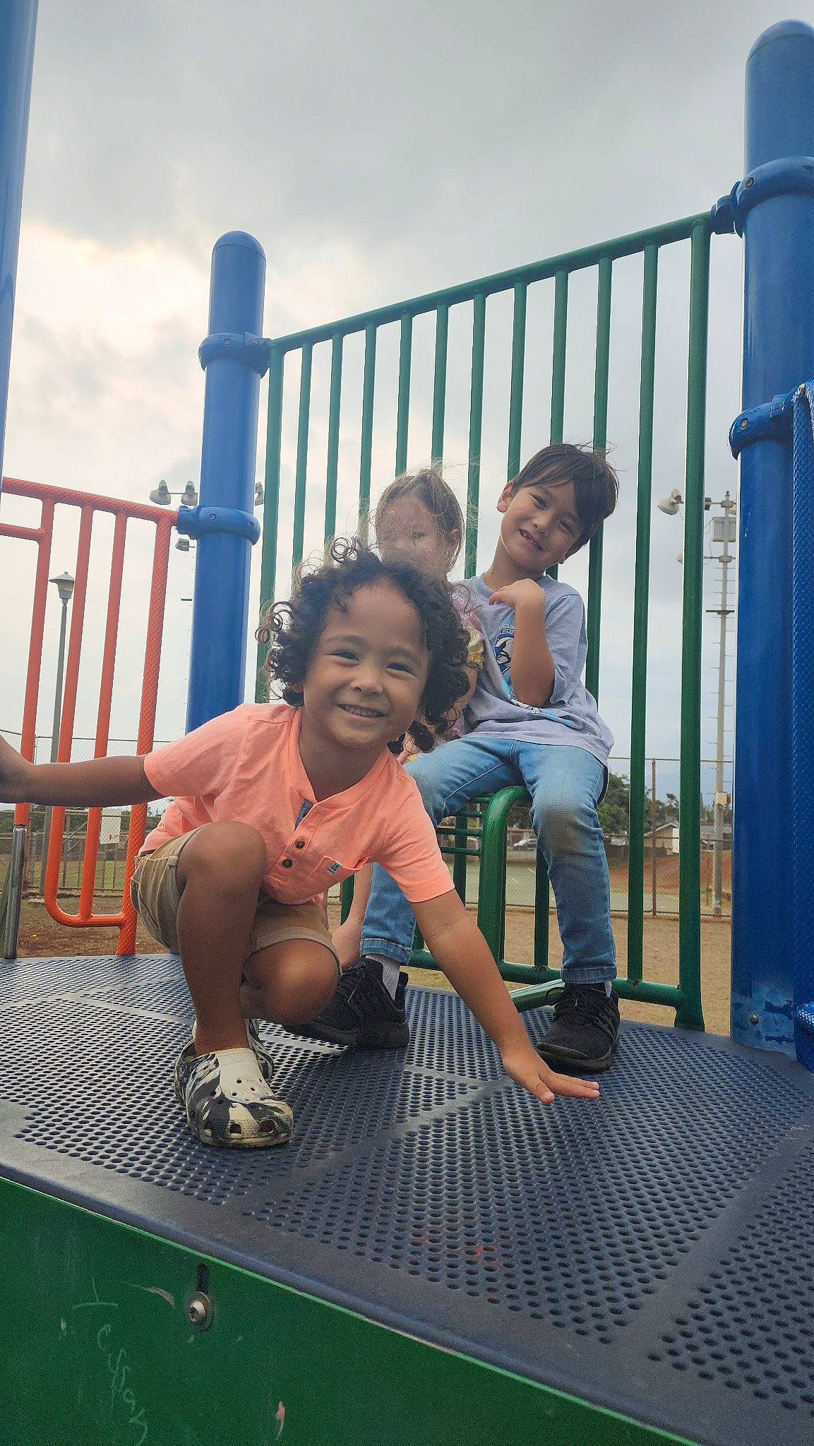 Blue is registered to the contest to win money with this photo: blue, child, city, cloud, event, fence, fun, grass, happy, joy, leisure, person, recreation, shorts, sitting, sky, smile, sneakers, t_shirt, toddler