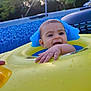 baby, child, pool, inflatable_ring, water, outdoor, summer, fun, floating, yellow, blue, hand, face, headrest, water_droplets, sunlight, trees, background, happy, playful