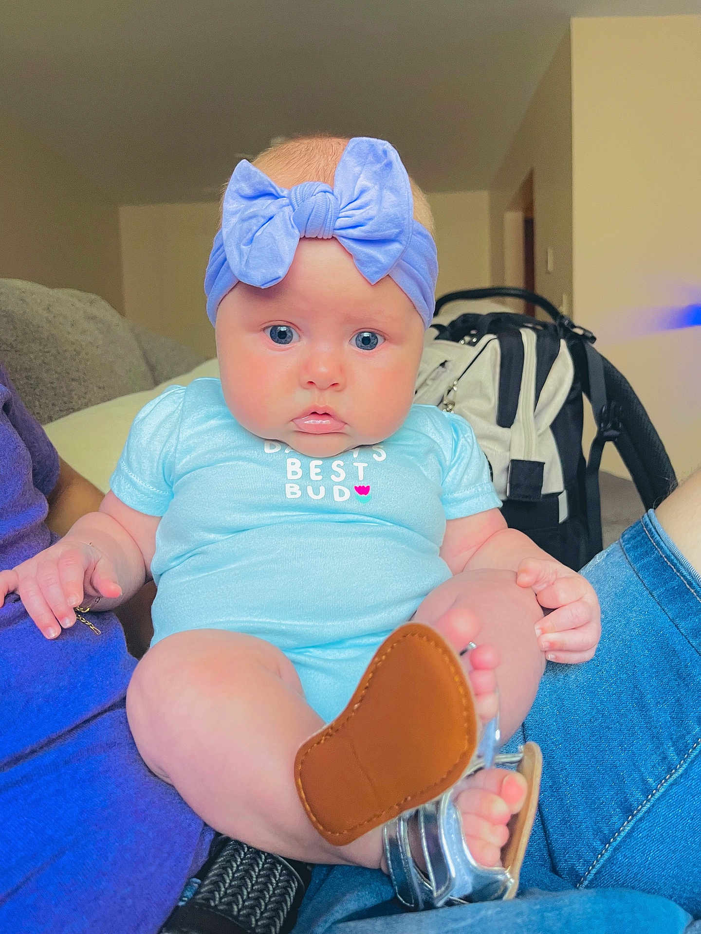 Noelymar joined the competition — help win amazing prizes! baby, child, blue_eyes, headband, bow, onesie, sitting, indoor, adult, lap, shoe, footwear, curious, person, cute, infant, clothing, skin, face, furniture