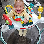 Zariyah joined the competition — help win amazing prizes! baby, infant, smiling, baby_walker, toy, indoor, floor, pink_bow, clothing, child, happy, person, play, seat, wood_floor, colorful, young, cute, hands, feet