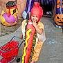 child, costume, hot_dog, shopping_cart, outdoor, halloween, pumpkin, pirate_duck, sidewalk, chalk_drawing, smiling, cute, playful, toy, festive, holiday, person, fun, colorful, celebration