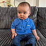 baby, child, blue_polo_shirt, jeans, black_shoes, couch, gray_couch, mirror, indoor, curious_expression, sitting, short_hair, casual_clothing, home_decor, furniture, portrait, young_child, pout, cute, person