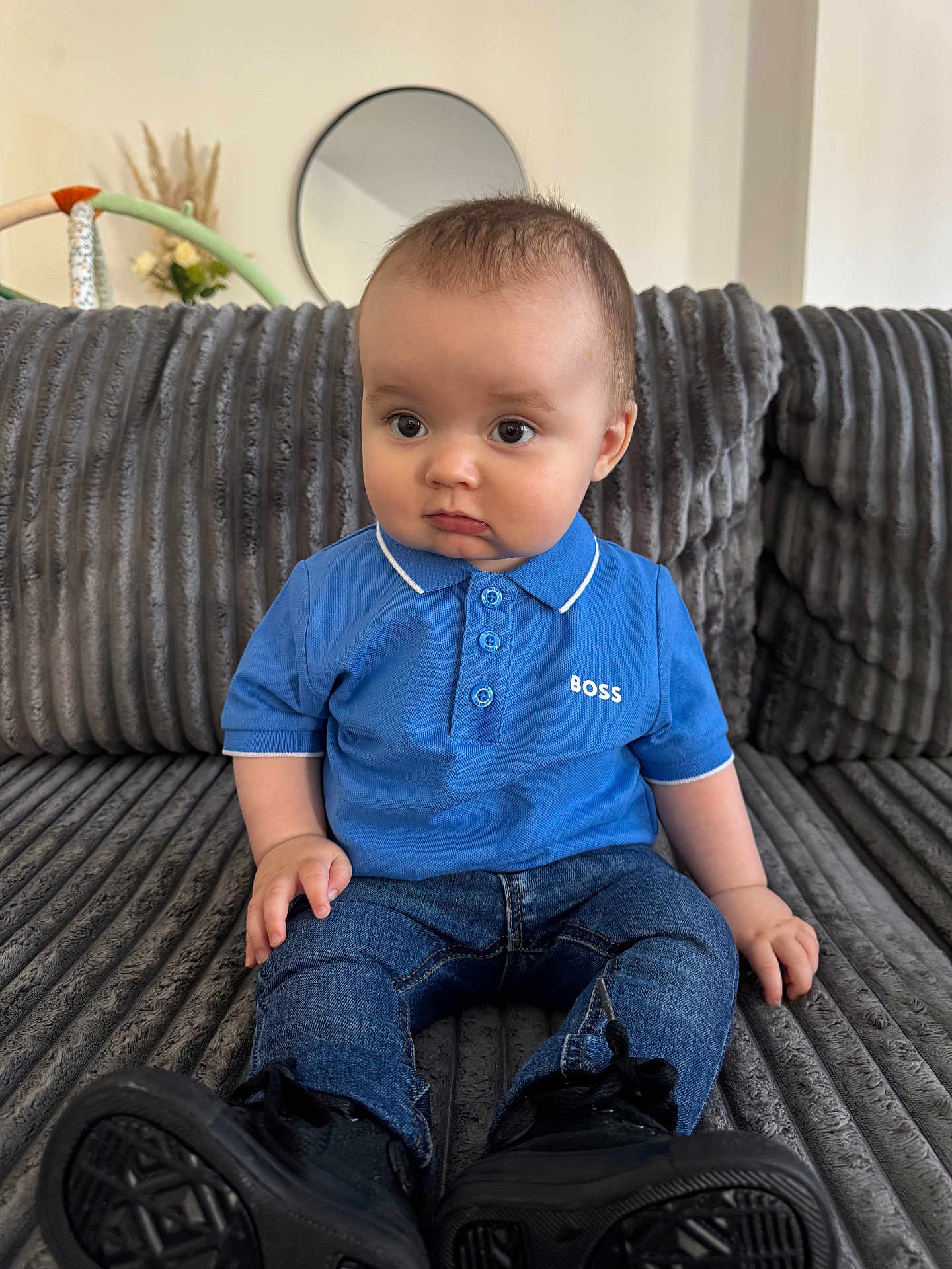 Mylan a rejoint le concours — aidez-le/la à gagner de superbes lots ! baby, child, blue_polo_shirt, jeans, black_shoes, couch, gray_couch, mirror, indoor, curious_expression, sitting, short_hair, casual_clothing, home_decor, furniture, portrait, young_child, pout, cute, person