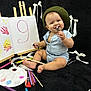 baby, child, smiling, beret, romper, marker, paint_palette, paint_tubes, paintbrush, canvas, handprints, black_background, sitting, art_supplies, colorful, playful, happy, indoors, portrait, creative