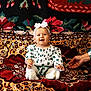 Lia a rejoint le concours — aidez-le/la à gagner de superbes lots ! baby, child, smiling, sitting, white_headband, white_clothing, patterned_clothing, hand, colorful_tapestry, floral_pattern, indoors, cute, happy, person, portrait, infant, soft_lighting, decor, warm_colors, family