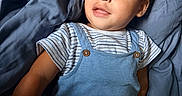 Leo is registered to the contest to win money with this photo: toddler, child, blue_overalls, striped_shirt, curly_hair, blue_blanket, indoor, portrait, cute, soft_texture, relaxed, baby, smiling, young_child, person, infant, casual_clothing, laying_down, light, skin