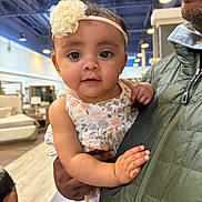 Ava Rose joined the competition — help win amazing prizes! baby, child, infant, person, adult, hand, face, headband, flower, dress, indoor, furniture, bed, lamp, floor, jacket, holding, curious, portrait, shopping