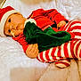 baby, infant, santa_hat, santa_costume, striped_pajamas, christmas, holiday, blanket, cozy, plush, lying_down, portrait, face, eyes, hand, skin, soft_texture, red_clothing, white_fur, nap_time