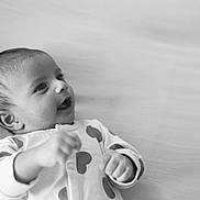 Krishika joined the competition — help win amazing prizes! baby, infant, black_and_white, smiling, lying_down, clothing, onesie, cute, face, portrait, happy, child, young, skin, head, expression, hands, indoor, soft_surface, newborn