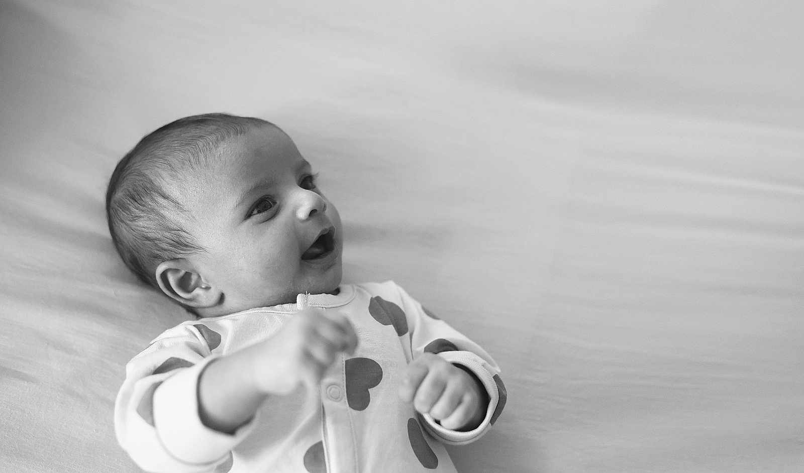 Krishika joined the competition — help win amazing prizes! baby, infant, black_and_white, smiling, lying_down, clothing, onesie, cute, face, portrait, happy, child, young, skin, head, expression, hands, indoor, soft_surface, newborn