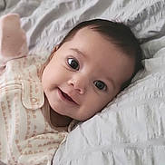 Marley is registered to the contest to win money with this photo: baby, infant, smile, face, eyes, blanket, clothing, bed, lying_down, cute, child, soft_light, portrait, closeup, sleepwear, happy, young, indoors, cozy, comfort