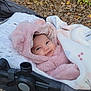 baby, infant, stroller, blanket, pink_clothing, hood, smile, face, outdoor, autumn_leaves, child, cute, warm_clothing, cozy, person, nature, bundle, happy, soft_texture, park