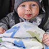 baby, child, infant, blanket, dinosaur_pattern, hat, gray_clothing, cute, tongue_out, smiling, seated, cozy, warm, portrait, face, hands, blue_eyes, indoor, plush, soft_texture
