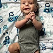 Jaxson joined the competition — help win amazing prizes! baby, smiling, onesie, grey_clothing, blanket, blue_pattern, construction_vehicles, infant, lying_down, hands_clasped, happy, cute, child, young_baby, indoor, soft_texture, toddler, portrait, playful, cheerful