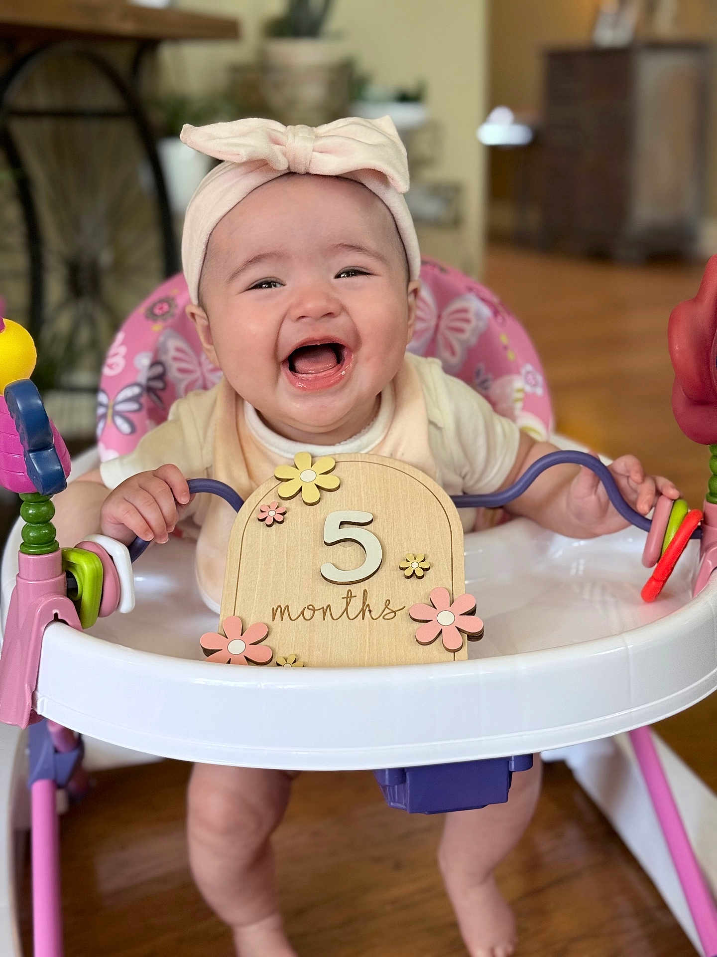 Leah joined the competition — help win amazing prizes! baby, infant, smiling, headband, walker, toy, milestone, 5_months, happy, cute, indoor, child, person, playing, pink, wooden_floor, closeup, face, hands, legs