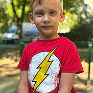Yanis a rejoint le concours — aidez-le/la à gagner de superbes lots ! child, boy, portrait, red_tshirt, lightning_bolt, outdoor, daylight, blonde_hair, blue_eyes, casual_clothing, park, fence, nature, young, person, expression, summer, greenery, background_blur, standing