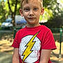child, boy, portrait, red_tshirt, lightning_bolt, outdoor, daylight, blonde_hair, blue_eyes, casual_clothing, park, fence, nature, young, person, expression, summer, greenery, background_blur, standing