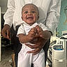 Jace is registered to the contest to win money with this photo: adult, baby, baby_gear, bow_tie, child, crib, face, furniture, happy, home, indoors, infant, nursery, parent, photography, portrait, room, smiling, standing, white_outfit