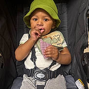 Jace joined the competition — help win amazing prizes!  안전, baby, bib, bucket_hat, child, close_up, gray_pants, green_hat, hand, harness, indoors, looking_at_camera, portrait, purple_object, seat_belt, seated, snack, stroller, toddler, white_shirt