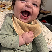 Kai joined the competition — help win amazing prizes! baby, child, smile, laugh, clothing, bib, green_outfit, indoor, cushion, patterned_blanket, happy, person, face, hand, infant, cute, portrait, baby_girl, expression, young
