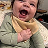 baby, child, smile, laugh, clothing, bib, green_outfit, indoor, cushion, patterned_blanket, happy, person, face, hand, infant, cute, portrait, baby_girl, expression, young