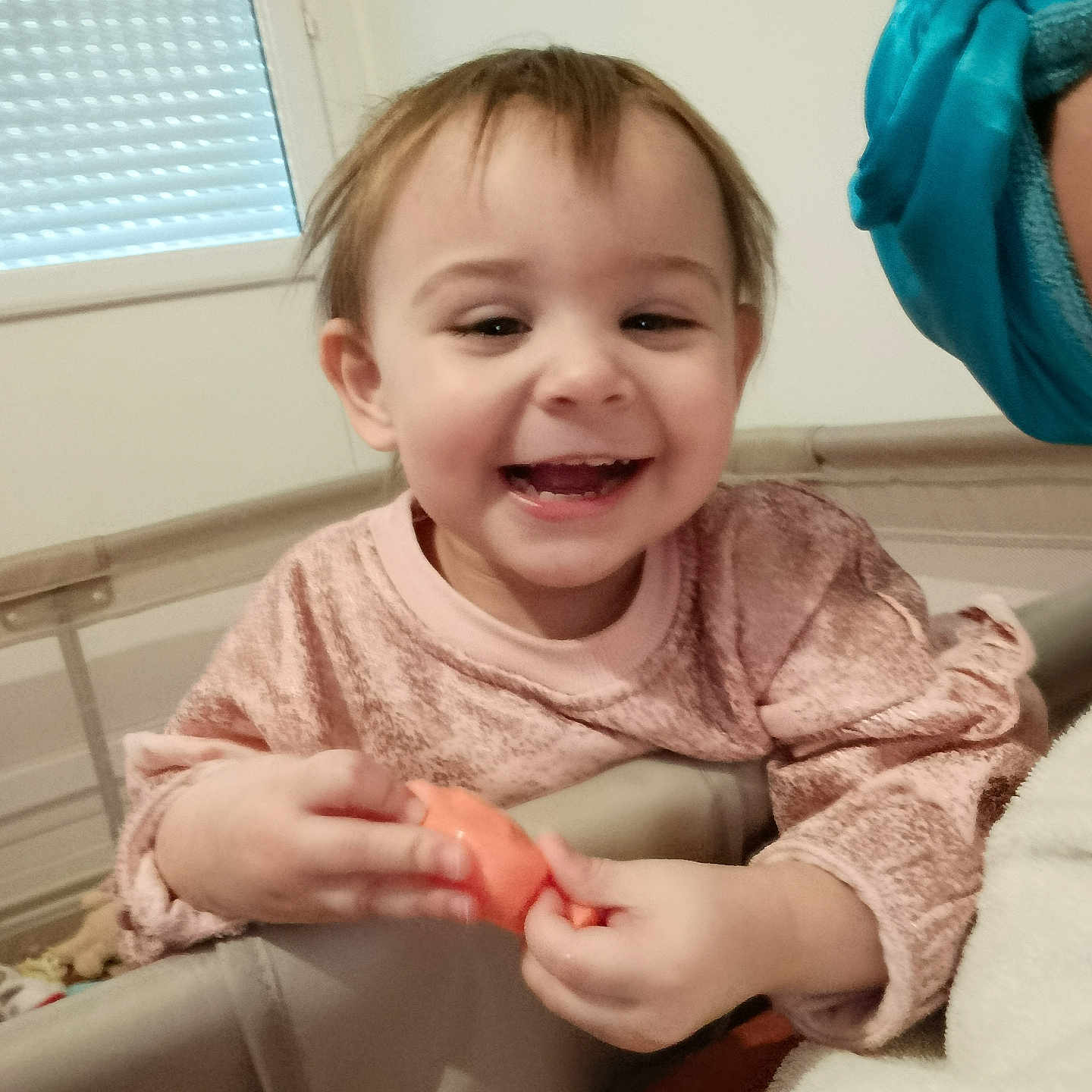 Mya participe au concours pour gagner de l'argent avec cette photo : toddler, child, smiling, indoor, toy, playpen, pink_sweater, happy, face, person, window, hair, hand, furniture, baby, cute, expression, young_child, holding, casual_clothing