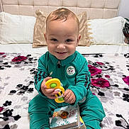 Ayden a rejoint le concours — aidez-le/la à gagner de superbes lots ! toddler, child, smiling, toy, board_books, bed, pillow, headboard, tracksuit, sneakers, indoor, happy, playing, seated, bedspread, floral_pattern, person, cute, young_child, casual_clothing