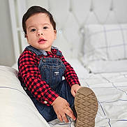 Thiago joined the competition — help win amazing prizes! toddler, child, bed, denim_overalls, red_checkered_shirt, shoe_sole, hand, face, indoor, pillow, blanket, white_bedding, curious, young_child, portrait, sitting, casual_clothing, cute, young_kid, home