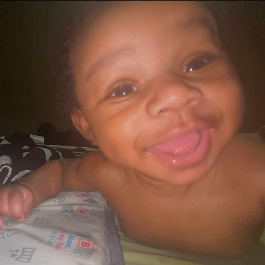 Neville joined the competition — help win amazing prizes! baby, bare_chested, bed, bedding, blanket, child, close_up, dark_background, face, flash, grinning, happy, home, indoor, infant, lying_down, photography, playful, portrait, smiling