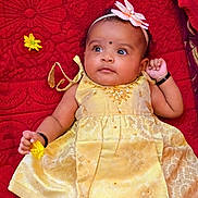 Amaris Hope joined the competition — help win amazing prizes! baby, infant, yellow_dress, flower, headband, red_blanket, cute, portrait, child, smiling, hand, face, lying_down, decorative_clothing, jewelry, black_bangle, indoors, soft_toys, happy, closeup