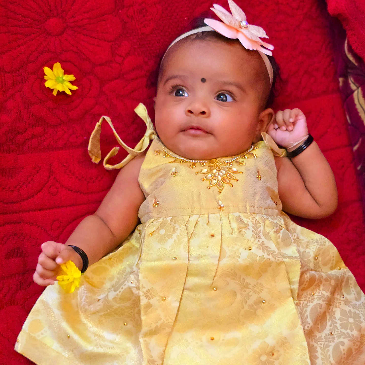 Amaris Hope joined the competition — help win amazing prizes! baby, black_bangle, child, closeup, cute, decorative_clothing, face, flower, hand, happy, headband, indoors, infant, jewelry, lying_down, portrait, red_blanket, smiling, soft_toys, yellow_dress