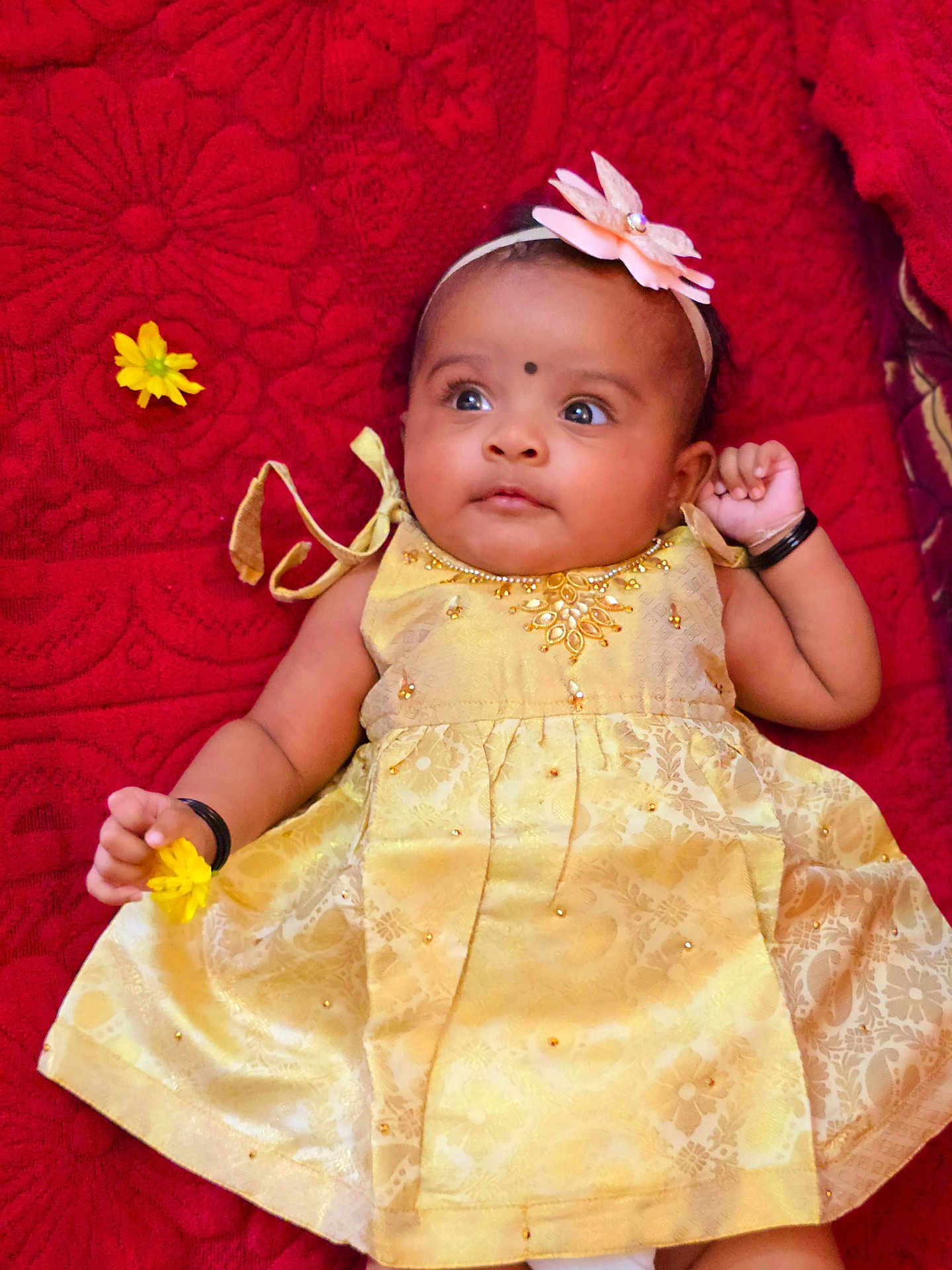 Amaris Hope joined the competition — help win amazing prizes! baby, infant, yellow_dress, flower, headband, red_blanket, cute, portrait, child, smiling, hand, face, lying_down, decorative_clothing, jewelry, black_bangle, indoors, soft_toys, happy, closeup