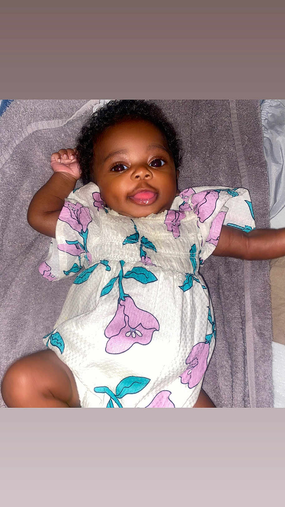 Raelyn is registered to the contest to win money with this photo: apparel, baby, bright, child, curly_hair, cute, face, floral_dress, happy, indoors, infant, lying_down, one_arm_up, portrait, skin, small_person, smiling, soft_surface, towel, young_child