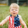 child, toddler, grass, outdoor, summer, romper, stars, stripes, american_flag, blue_eyes, blond_hair, cute, smiling, sitting, baby, nature, playful, portrait, casual, sunlight