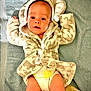 baby, infant, robe, hood, towel, diaper, lying_down, face, eyes, skin, cute, soft_texture, patterned_clothing, child, indoors, expression, person, newborn, cozy, blanket
